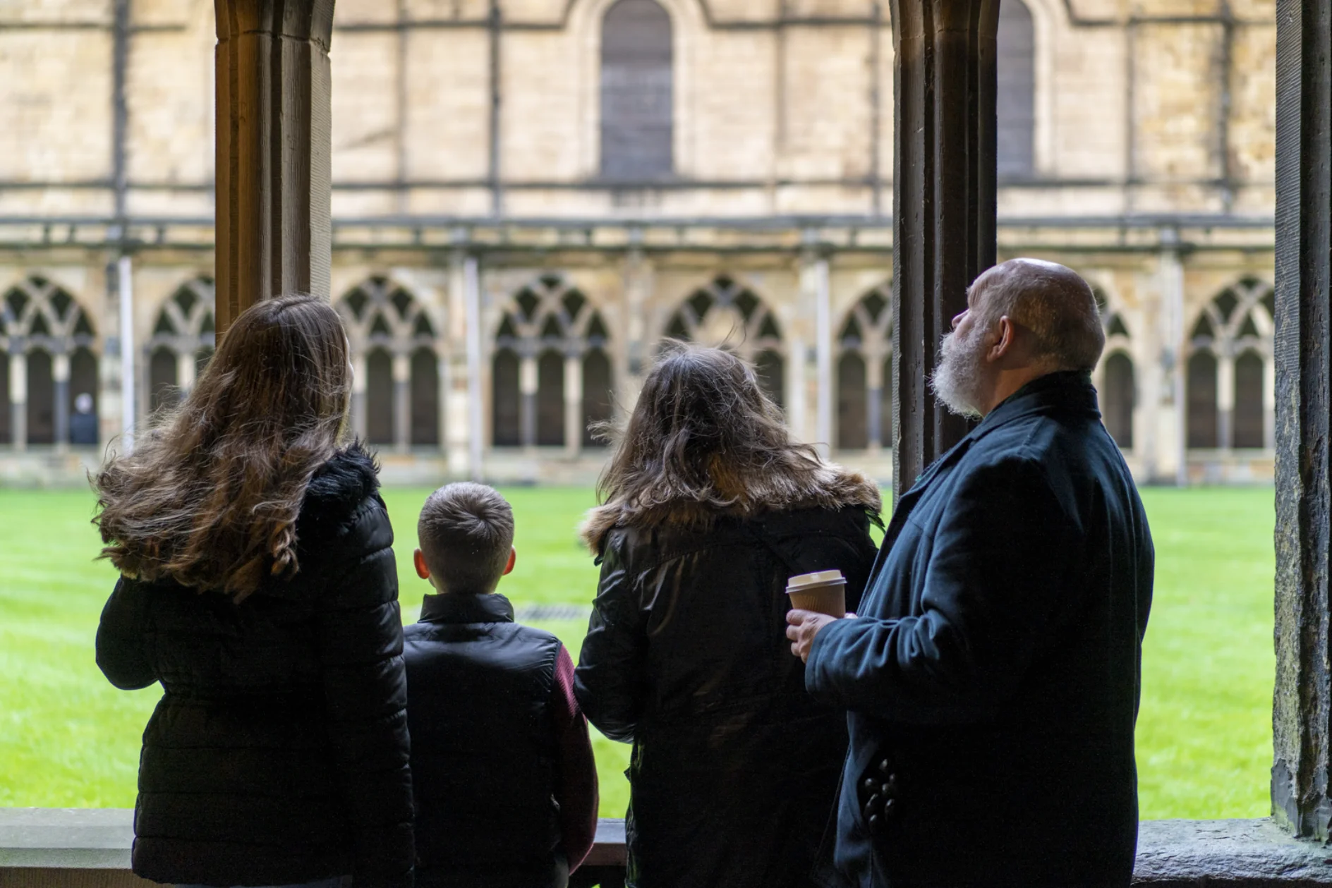 A family of four in the cloisters looking onto Durham Cathedral's cloister garth